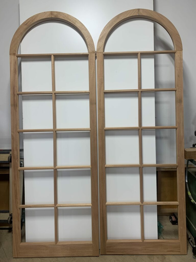 Two Arched Wooden Doors With White Trim, Leading To a Traditional European-Style Building.